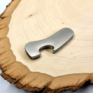 Pode incluir: Um abridor de garrafas prateado com um design liso e curvo. O abridor é feito de metal e tem um pequeno furo para abrir garrafas.