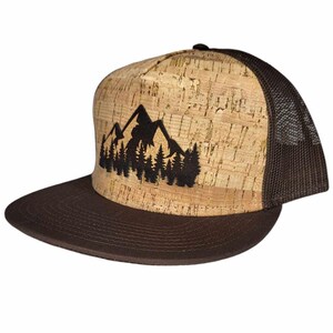 Puede incluir: Una gorra de camionero de corcho marrón y beige con un diseño de silueta de montaña negra. La gorra tiene una parte trasera de malla marrón.