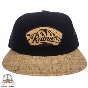 Puede incluir: Una gorra de béisbol negra y marrón con una visera de corcho y un parche de corcho con el texto "Mt Rainier" y una silueta de montaña.