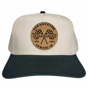 May include: A beige and black baseball cap with a cork patch featuring a checkered flag design and the text "DREAM CRUISE Woodward EST. 1995 DETROIT, MI".