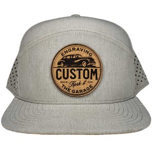 May include: A gray and brown baseball cap with a cork patch featuring a vintage car and the text "Engraving Custom Kork It The Garage Since 2021".