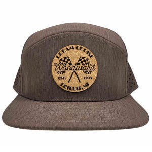 May include: A brown baseball cap with a cork patch featuring the text "Dream Cruise Woodward Est. 1995 Detroit, MI" and a graphic of two checkered flags.