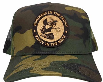 Puede incluir: Una gorra de camionero de camuflaje con un parche de cuero marrón que presenta un pato de dibujos animados con gafas de sol y un cigarrillo. El parche dice "Business in the front, Party in the back."