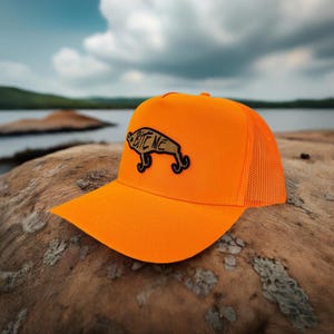 May include: Orange and black trucker hat with a fishing lure patch that says "Bite Me".