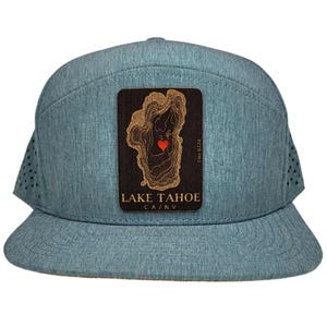 May include: A light blue cap with a flat brim and a perforated side panel. The cap features a wooden patch with a map of Lake Tahoe, a red heart, and the text "LAKE TAHOE CA/NV". The elevation is noted as Elev 6224.