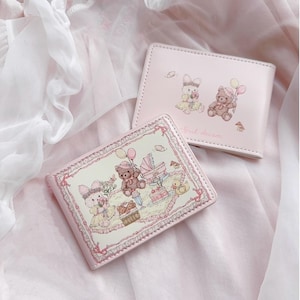 May include: Two pink wallets with illustrations of teddy bears and bunnies. One wallet features a scene with a baby carriage, cake, and balloons. The other wallet has two bears and the words "Girl dream".