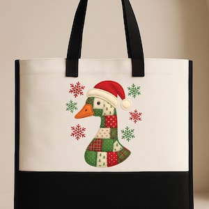 May include: A canvas tote bag with a black base and handles. The upper portion is white, featuring a goose wearing a Santa hat and a patchwork design in green, red, and white. Red and green snowflakes surround the goose. The text "CUSTOM TEE HAUS" is in the lower left corner.
