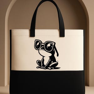 May include: A two-tone tote bag with a black and cream color scheme. The upper cream section features a black and white illustration of a frog wearing sunglasses. The bag has black handles and the text "CUSTOM TEE HAUS" is in the lower left corner.