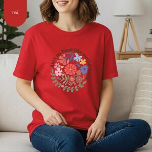 Peut inclure: T-shirt rouge avec un motif de couronne florale et le texte "Ain't no hood like motherhood". La couronne est compos&eacute;e de fleurs color&eacute;es et de feuilles vertes. Le t-shirt est en mati&egrave;re douce et convient &agrave; un usage quotidien.