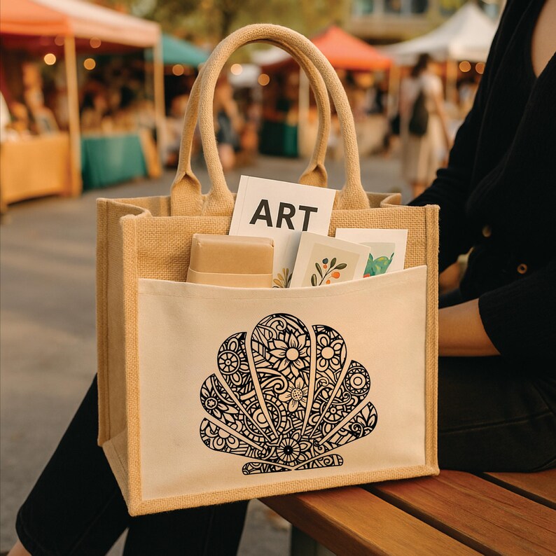 May include: A beige tote bag with a white pocket featuring a black seashell design. The bag has two handles and contains a card that says "ART". The bag is filled with art supplies and is perfect for carrying art supplies.