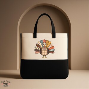 K&ouml;nnte beinhalten: Eine zweifarbige Tragetasche mit schwarzem Boden und cremefarbenem Oberteil. Die Tasche zeigt eine farbenfrohe Truthahn-Illustration mit Patchwork-Design. Der Truthahn hat einen karierten K&ouml;rper und einen lebendigen Federf&auml;cher. Schwarze Griffe runden das Design ab.