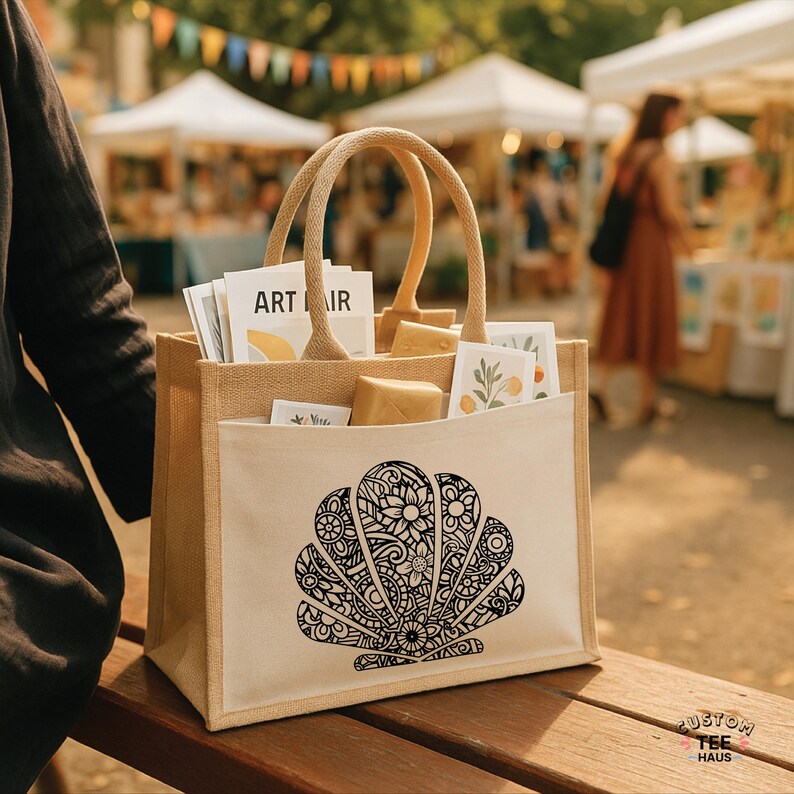 May include: A beige tote bag with a large black and white seashell design on the front. The bag has a light beige pocket and handles. The bag is filled with various items, including art prints and small packages. The text "ART IR" is visible.