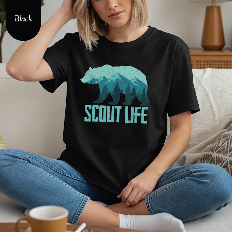 Puede incluir: Camiseta negra con un dise&ntilde;o de oso turquesa que incorpora monta&ntilde;as y &aacute;rboles. El texto "SCOUT LIFE" est&aacute; impreso debajo. La camiseta est&aacute; hecha de un material suave.