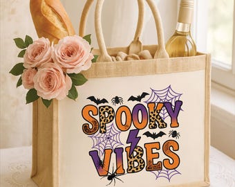 Könnte beinhalten: Beige Tragetasche mit den Worten "Spooky Vibes" in Orange und Lila, verziert mit Fledermäusen, Spinnen und Spinnweben. Die Tasche enthält ein Baguette, eine Weinflasche und rosa Rosen.