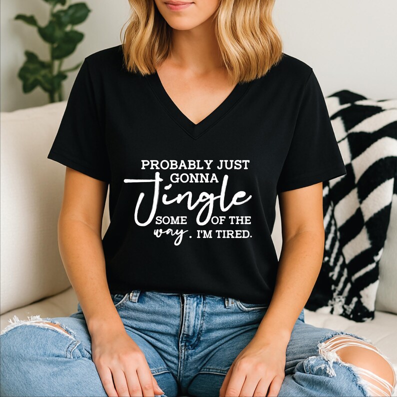 May include: Black V-neck t-shirt with the text "Probably just gonna jingle some of the way. I'm tired." in white script. The shirt is paired with blue jeans. The overall theme is casual wear.