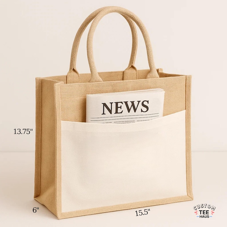 May include: A beige jute tote bag with a white front pocket, holding a newspaper with the word "NEWS". The bag is 13.75 inches tall, 15.5 inches wide, and 6 inches deep, with beige handles. The bag has the text "CUSTOM TEE HAUS" on the bottom right.