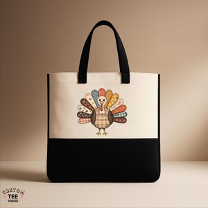 K&ouml;nnte beinhalten: Eine zweifarbige Tragetasche mit einem Truthahn-Design. Der obere Teil ist cremefarben, der untere Teil ist schwarz. Die Truthahn-Illustration hat einen karierten K&ouml;rper und einen bunten, gemusterten Schwanz. Schwarze Griffe.