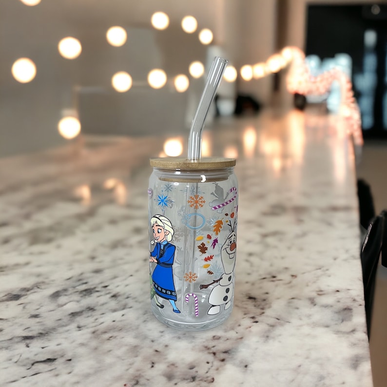 Puede incluir: Un vaso de vidrio transparente con una tapa de madera y una pajita. El vaso tiene un dise&ntilde;o con Elsa y Olaf de la pel&iacute;cula Frozen. El dise&ntilde;o incluye copos de nieve, bastones de caramelo y hojas de oto&ntilde;o.