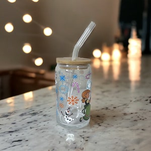 Puede incluir: Un vaso de vidrio transparente con tapa de bamb&uacute; y una pajita. El vaso tiene un dise&ntilde;o de invierno con copos de nieve, bastones de caramelo y personajes de la pel&iacute;cula Frozen.