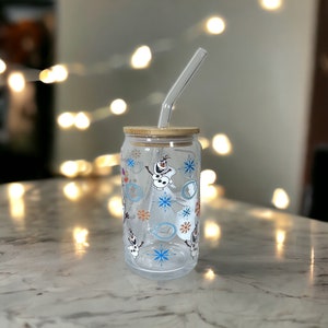 Puede incluir: Un vaso de vidrio transparente con tapa de bamb&uacute; y una pajita. El vaso tiene un patr&oacute;n de Olaf de Frozen, copos de nieve y remolinos.