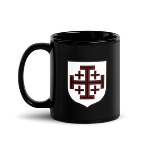 Pode incluir: Caneca de café de cerâmica preta com um escudo branco que apresenta uma cruz vermelha com quatro cruzes vermelhas menores dentro. O escudo está sobre um fundo preto.