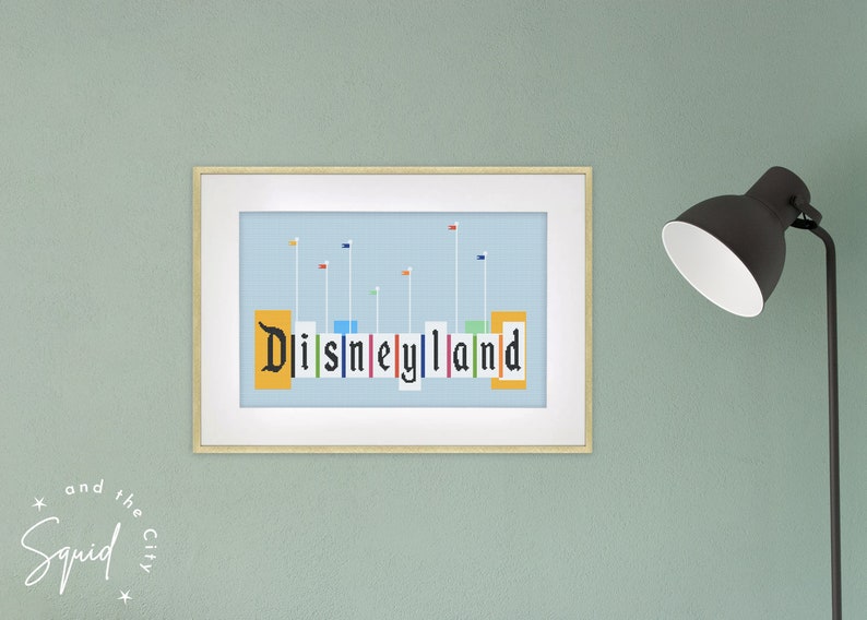 Puede incluir: Una impresi&oacute;n enmarcada de una ilustraci&oacute;n estilizada del letrero de Disneyland con banderas de colores. El letrero est&aacute; formado por bloques individuales con las letras "Disneyland" en negro.