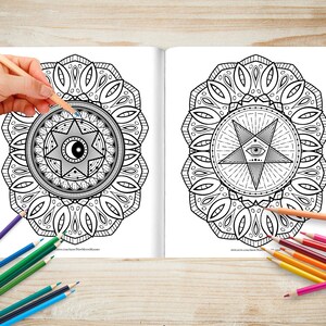 May include: A colouring book with two pages featuring intricate mandala designs. The mandalas are black and white and feature a star with an eye in the centre. The book is open and a hand is holding a blue coloured pencil over the mandala on the left page.