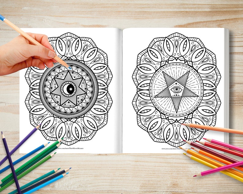 May include: A colouring book with two pages featuring intricate mandala designs. The mandalas are black and white and feature a star with an eye in the centre. The book is open and a hand is holding a blue coloured pencil over the mandala on the left page.