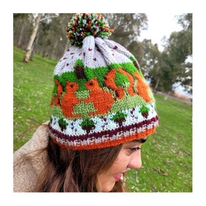 May include: A knitted hat with a pom pom on top. The hat features a colourful pattern of squirrels, trees, and leaves. The hat is made of a soft, warm yarn and is perfect for keeping your head warm in the winter.