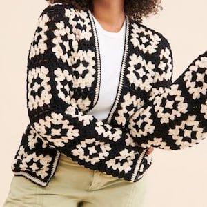 May include: A black and white crochet cardigan with a granny square pattern. The cardigan has a long sleeve and a relaxed fit.