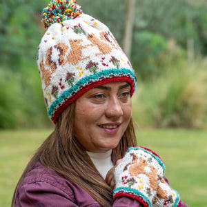 May include: White knitted hat with a pom-pom on top and a brown squirrel pattern. The hat has a red, white, and blue trim. The hat is being worn by a person.