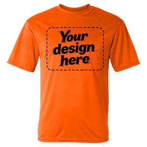 May include: A bright orange short-sleeved t-shirt featuring a central rectangular area outlined with a black dashed line. Inside this box, the black text reads Your design here in a bold, stylized font, centered on the front of the garment.