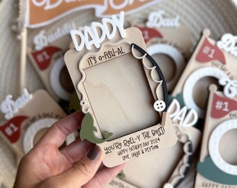 May include: A wooden photo frame with a fish design and the text "It's O-Fish-Al" and "You're Reel-Y The Best! Happy Father's Day 2024 Love, Lukas & Peyton".