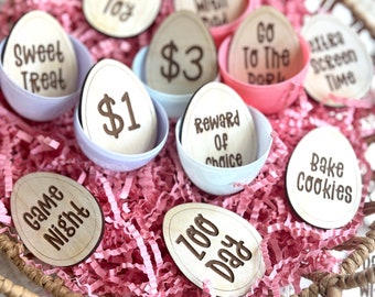May include: A wicker basket filled with pink crinkle paper and wooden Easter eggs. The eggs have various phrases written on them, including "Game Night", "Zoo Day", "Stay Up", "Dinner", "$1", "$3", "Sweet Treat", "New Toy", "Go To The Park", "Reward Of Choice", "Extra Screen Time", and "Bake Cookies".