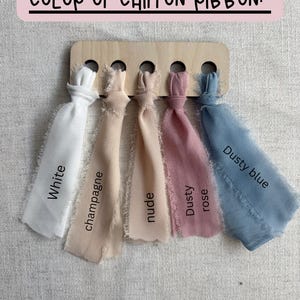 May include: A wooden display board with five chiffon ribbon samples in white, champagne, nude, dusty rose, and dusty blue. Each ribbon is labeled with its color name. The text "COLOR OF CHIFFON RIBBON:" is at the top.