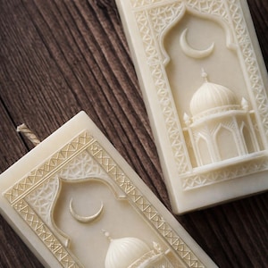 Puede incluir: Dos velas rectangulares de color crema con intrincados diseños de mezquita y luna creciente. Las velas tienen una superficie texturizada y un borde decorativo. Cada vela tiene una mecha de fibra natural.