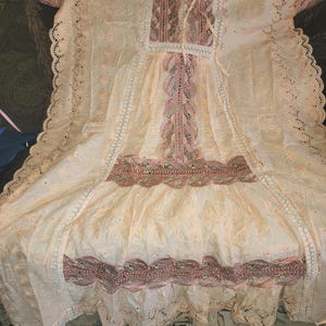 May include: A white cotton dress with pink and green embroidery. The dress has a lace trim and a gathered skirt.