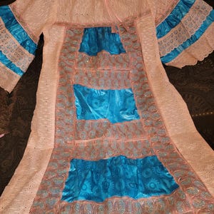 May include: A long, pink dress with blue satin panels and intricate lace detailing. The dress has a round neckline and long sleeves with lace cuffs.
