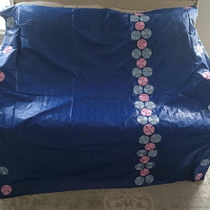May include: A navy blue textile with a repeating pattern of small circles and a vertical line of alternating pink and light blue floral designs. The fabric is draped over a surface, showcasing its texture and design.