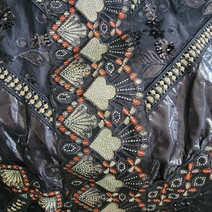 May include: Black fabric with intricate embroidery featuring silver and orange details. The design includes geometric shapes and floral motifs.