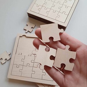 May include: A wooden jigsaw puzzle with a natural finish. The puzzle is made up of 25 pieces and is in the shape of a square. The pieces are loose and are being held in a hand.