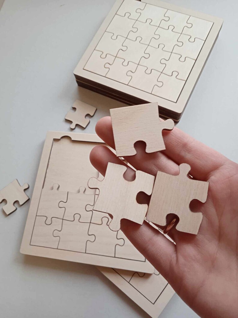 May include: A wooden jigsaw puzzle with a natural finish. The puzzle is made up of 25 pieces and is in the shape of a square. The pieces are loose and are being held in a hand.