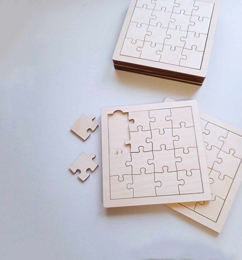 May include: Two unfinished wooden jigsaw puzzles, one with a piece missing. The puzzles are made of light brown wood and have a white background. The puzzles are square and have a simple design.