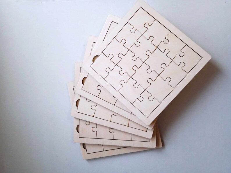 May include: A stack of five unfinished wooden jigsaw puzzles, each with a different number of pieces. The puzzles are all the same size and shape, and they are all made of light-colored wood.