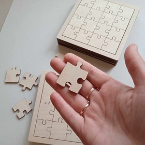 May include: A wooden jigsaw puzzle with a single piece removed and held in a hand. The puzzle is made of light wood and has a simple design. The piece is also made of light wood and has a simple design.