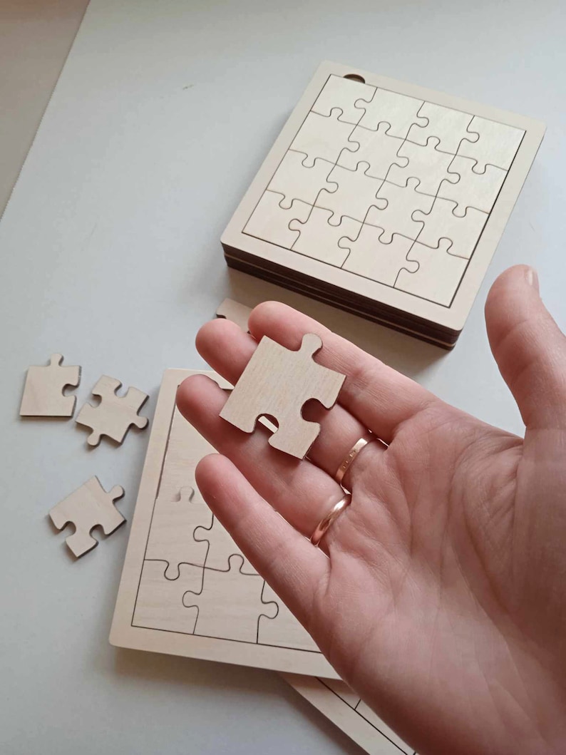 May include: A wooden jigsaw puzzle with a single piece removed and held in a hand. The puzzle is made of light wood and has a simple design. The piece is also made of light wood and has a simple design.