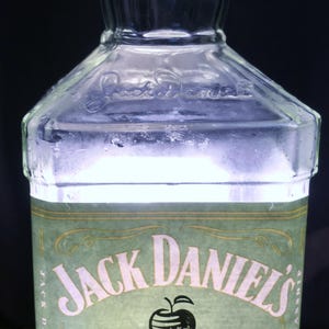 Könnte beinhalten: Eine klare Glasflasche Jack Daniel's Tennessee Apple Likör. Das Etikett ist grün mit goldenen Akzenten und zeigt den Markennamen, eine schwarze Apfelgrafik und die Worte "Tennessee Apple". Die Flasche ist 700 ml und 35 % vol.