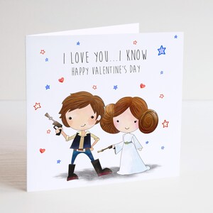 May include: A Valentine's Day card with cartoon illustrations of a male and female character holding blasters. The card reads "I LOVE YOU... I KNOW HAPPY VALENTINE'S DAY" with red hearts and blue stars scattered around the characters.