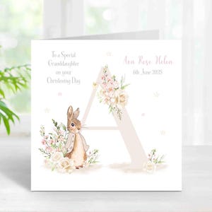 May include: A christening card featuring a watercolour illustration of a bunny and floral elements. The card includes the letter "A" and the text "To a Special Granddaughter on your Christening Day" and "Ava Rose Helen 6th June 2025".