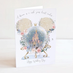 May include: A white wedding card with a fairytale castle in a snow globe, floral decorations, and the text "A dream is a wish your heart makes..." and "Happy Wedding Day". The card is shaped like a Mickey Mouse head.